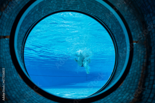Woman Swimming in the Ship Porthole in Underwater in Swimming Pool in a Sunny Day in Switzerland.