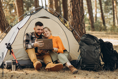 Couple sitting in tent in forest working on laptop