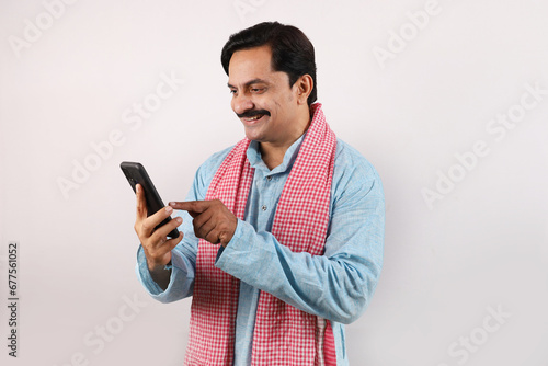 portrait of happy Indian farmer man in rural India concept. white background. Cheerful farmer looking into the mobile phone screen, using advanced technology.
