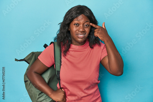 Curvy traveler with backpack in studio showing a disappointment gesture with forefinger.