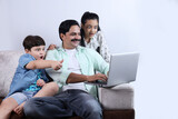 Happy Indian family of father, son and daughter surfing laptop having pleasant time together joyfully. Family is looking into the laptop, surprised, shocked. 