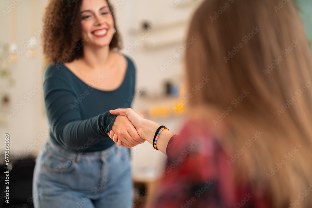 Happy young females in casual clothes smiling and shaking hands while greeting each other during meeting against blurred background Happy young females in casual clothes smiling and shaking hands while greeting each other during meeting against blurred background
