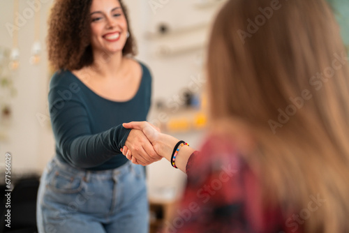 Happy young females in casual clothes smiling and shaking hands while greeting each other during meeting against blurred background photo