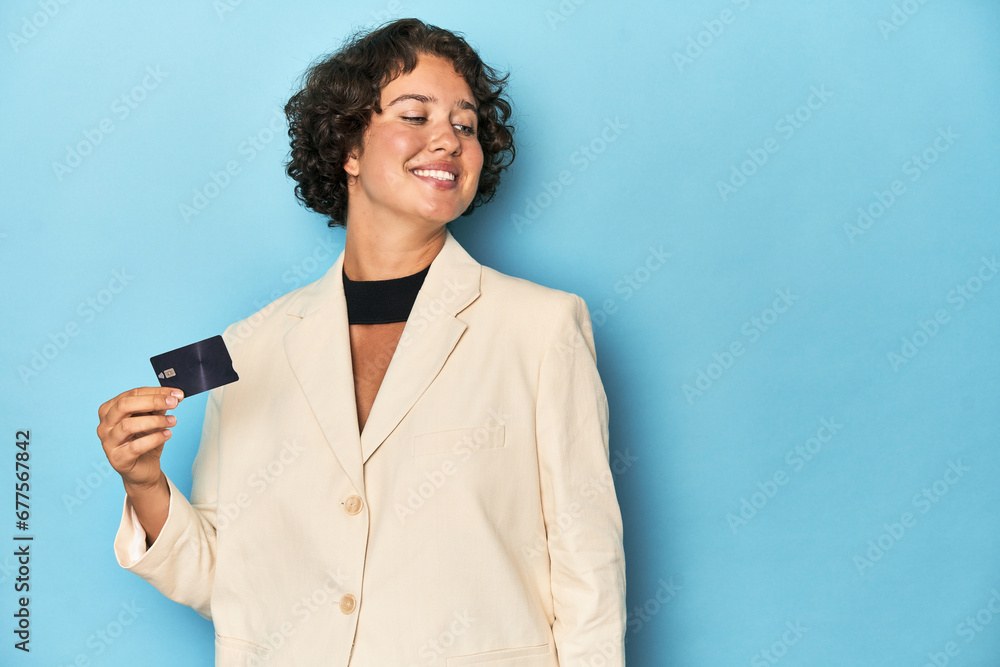 Young woman with credit card, elegant white blazer looks aside smiling, cheerful and pleasant. Young woman with credit card, elegant white blazer looks aside smiling, cheerful and pleasant.