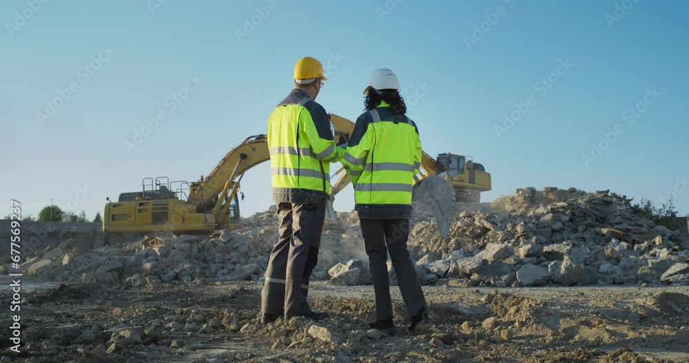 Back View Of Hispanic Female Project Manager And Caucasian Male Civil Engineer Discussing New Real Estate Project On Construction Site. Colleagues Talking About Urban Planning Of New City District . Back View Of Hispanic Female Project Manager And Caucasian Male Civil Engineer Discussing New Real Estate Project On Construction Site. Colleagues Talking About Urban Planning Of New City District .