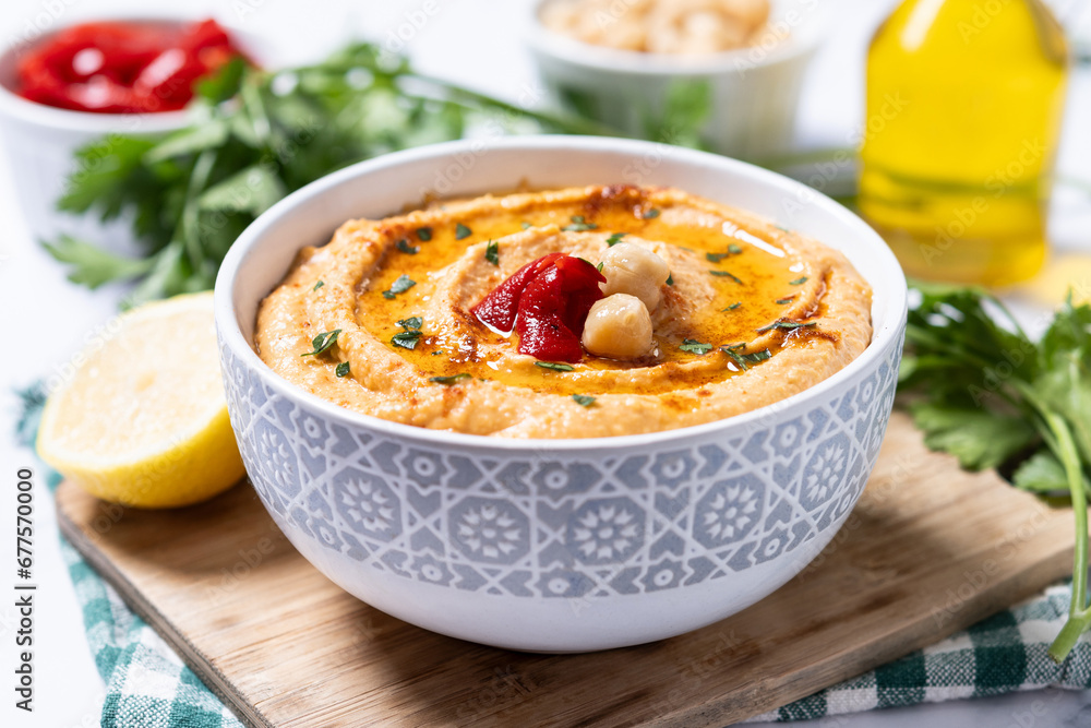 Roasted red pepper hummus in white bowl on white marble background.