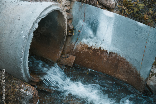 Wastewater and sewage flow from a pipe into a polluted river, creating a bad smell and a chemical hazard. The photo illustrates the environmental impact of industrial waste and poor drainage system. photo