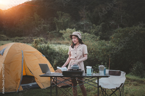 Happy woman freelancer traveller working online using laptop ,take photo and drink a cup coffee or tea enjoying the beautiful camping tent landscape with mountain is holiday relaxed lifestyle concept.