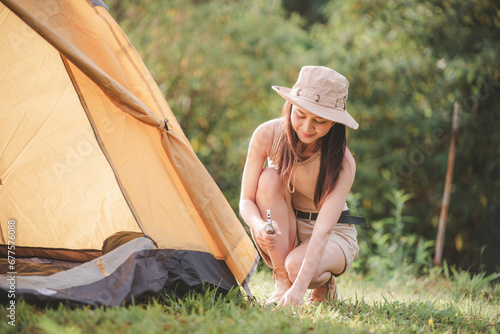 Woman setting up tent at camp site Pulls and sticks a metal tent peg into the ground is holiday activity with mountain nature lifestyle concept. photo