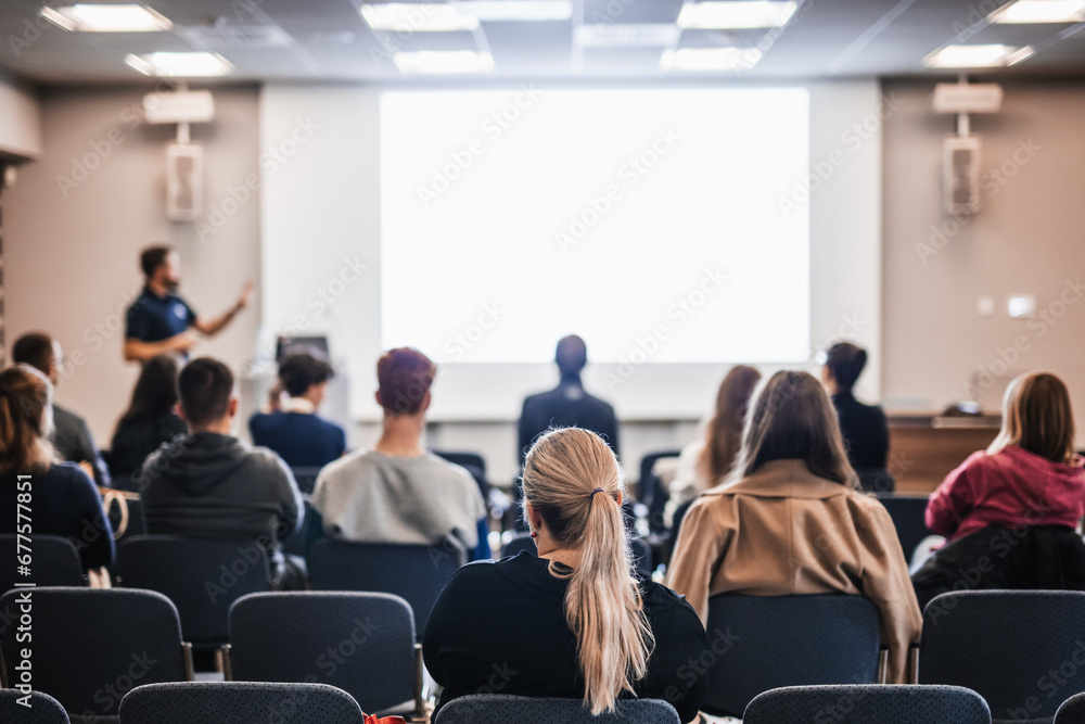 Fototapeta premium Speaker giving a talk in conference hall at business event. Rear view of unrecognizable people in audience at the conference hall. Business and entrepreneurship concept