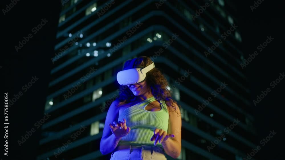Low angle shot multi racial young woman working outside at modern company office building night background. Girl wearing VR glasses moving hands in air, typing on imagine keyboard in cyber space 4K Low angle shot multi racial young woman working outside at modern company office building night background. Girl wearing VR glasses moving hands in air, typing on imagine keyboard in cyber space 4K