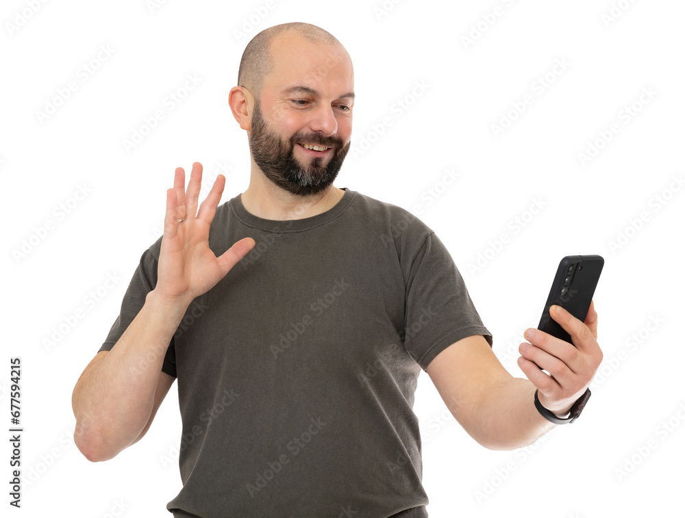 Portrait oh happy man with beard wearing brown t-shirt take selfie and waving raised palm, isolated on white background. Bald guy holding cell phone and say HI, HELLO, greeting you, welcoming guests. Portrait oh happy man with beard wearing brown t-shirt take selfie and waving raised palm, isolated on white background. Bald guy holding cell phone and say HI, HELLO, greeting you, welcoming guests.