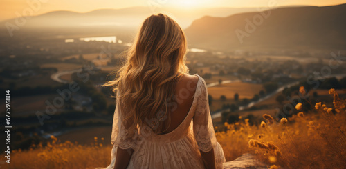 Girl seen from behind alone who is sitting on top of a hill looking towards the valley, warm colors soft tones.