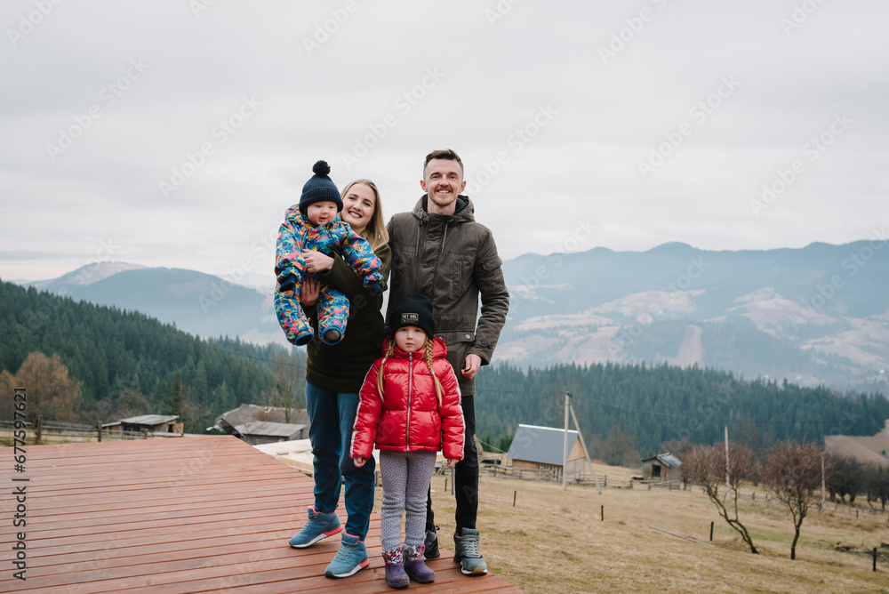 Family vacation with children in mountains. Mother, father embrace kids on terrace on an autumn day. People standing in backyard of country house. Mom, dad hug daughter, son enjoy time together.