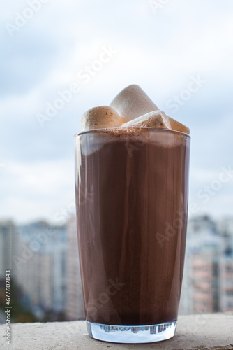 Hot coffee latte with marshmello in a glass which stands against the backdrop of a busy city. Chilling in weekend