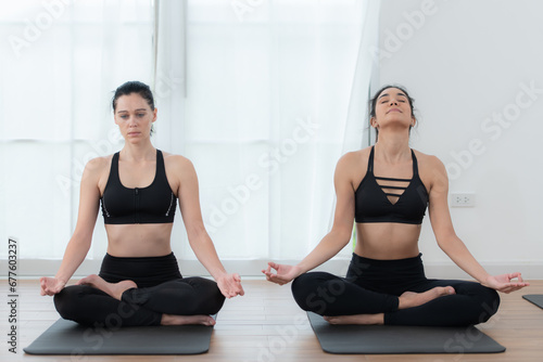 Two young woman meditating in lotus pose on exercise mat at home, Yoga exercise concept