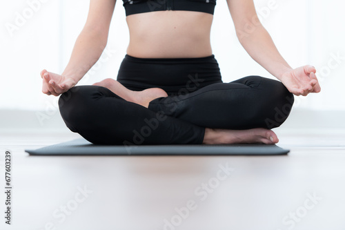 Mid section of woman meditating in lotus pose on exercise mat at home, Yoga exercise concept