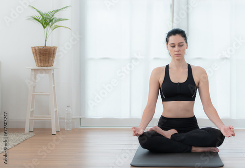 Fototapeta Naklejka Na Ścianę i Meble -  Young woman meditating in lotus pose on exercise mat at home, Yoga exercise concept