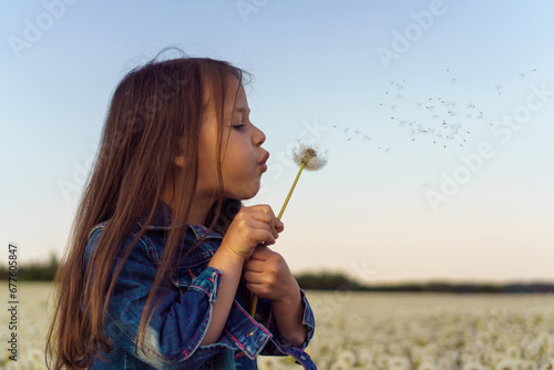 Loveable girl carefully hold white dandelion and blowing seeds of flower, walking in field. Tassels flying through air.