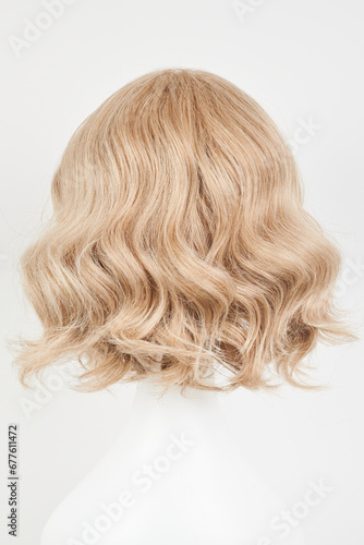 Natural looking blonde fair wig on white mannequin head. Middle length hair cut on the plastic wig holder isolated on white background, back view