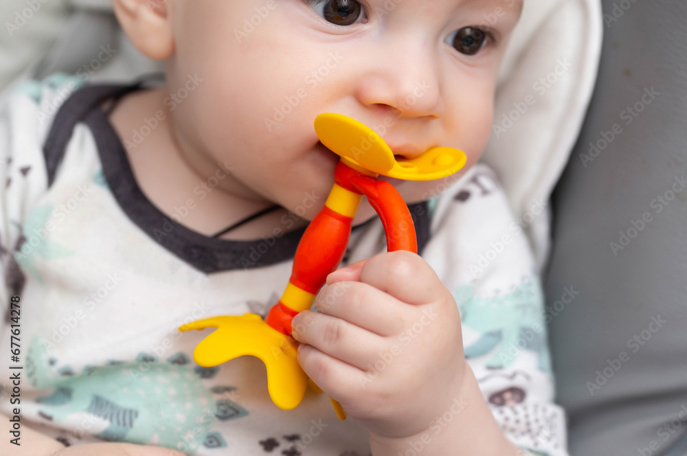 A child caucasian boy at the age of one year bites a dental toy massager teether. Itching of the gums and salivation from the mouth in children during teething. A child caucasian boy at the age of one year bites a dental toy massager teether. Itching of the gums and salivation from the mouth in children during teething.