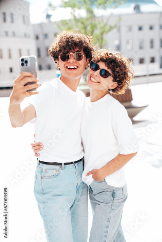 Young smiling beautiful woman and her handsome boyfriend in casual summer white t-shirt and jeans clothes. Happy cheerful family. Female having fun. Couple posing in street at sunny day. Take selfie