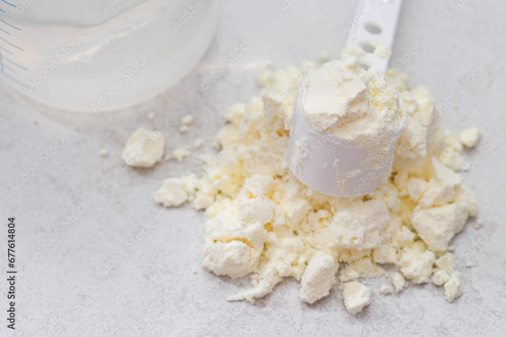 A baby feeding bottle and a measuring spoon with a handful of dry baby formula for preparing milk for the baby. Useful and healthy food, close-up A baby feeding bottle and a measuring spoon with a handful of dry baby formula for preparing milk for the baby. Useful and healthy food, close-up