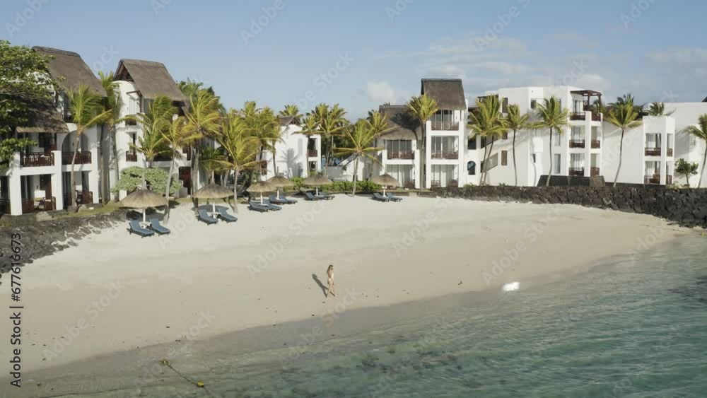 Aerial view of a woman on the beach along the shore with umbrellas at sunset, Ilot Lievres, Trou d'Eau Douce, Flacq district, Mauritius. Aerial view of a woman on the beach along the shore with umbrellas at sunset, Ilot Lievres, Trou d'Eau Douce, Flacq district, Mauritius.
