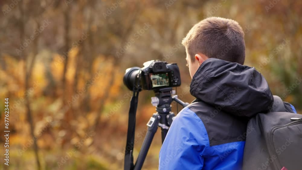 A young boy, camera in hand, photographs a tranquil autumn-winter woodland with a meandering stream. Exploring outdoor photography. A young boy, camera in hand, photographs a tranquil autumn-winter woodland with a meandering stream. Exploring outdoor photography.