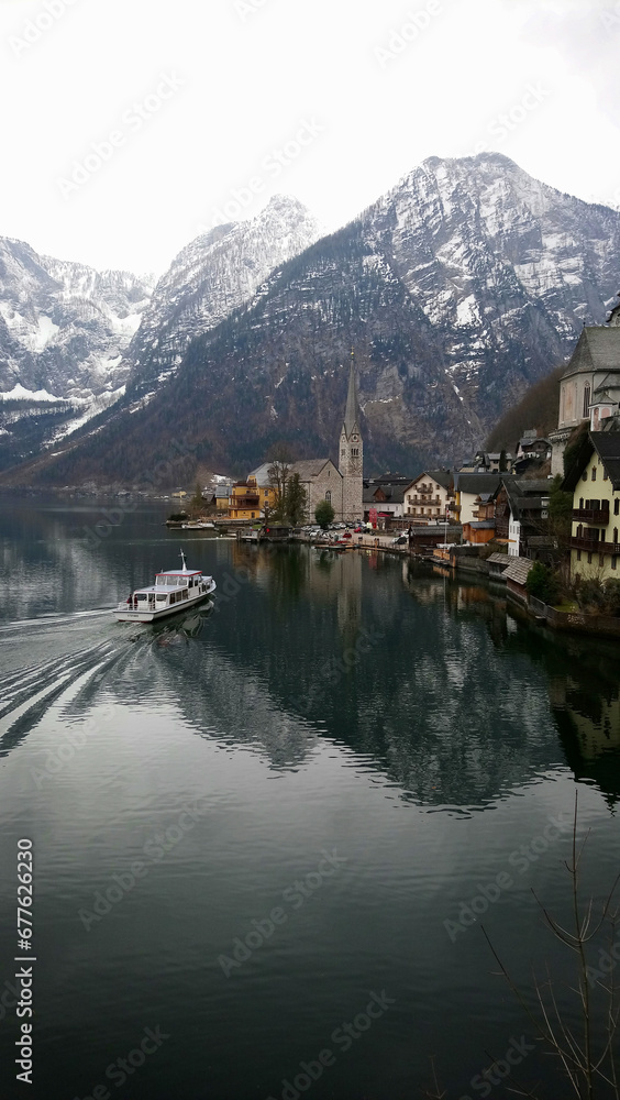 Naklejka premium Serene Hallstatt village in March, a tranquil haven with a mirror-like lake reflecting the alpine splendor; a quaint, peaceful town, whispering history beneath the majestic, undisturbed Alps.