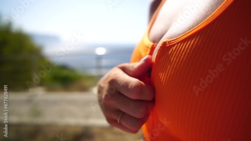 Close-up of chest area of an unrecognizable young woman. She unzips her orange sport clothes to cool down after workout. Zipper on the woman's sportswear open by itself on her chest. Slow motion