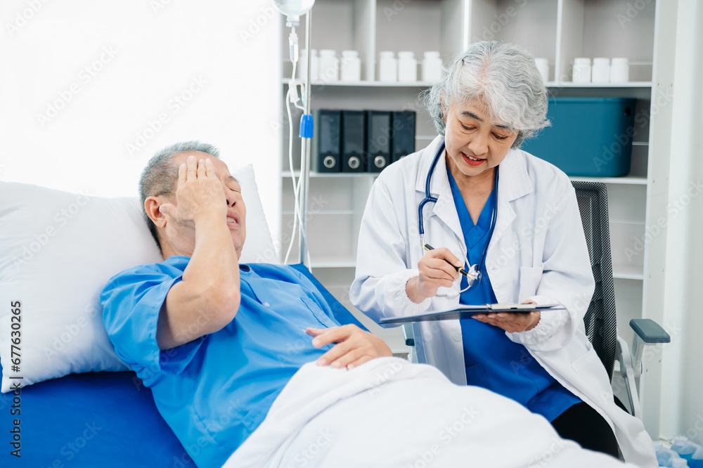 Asian doctor in white suit take notes while discussing and Asian elderly, man patient who lying on bed with receiving saline solution Asian doctor in white suit take notes while discussing and Asian elderly, man patient who lying on bed with receiving saline solution