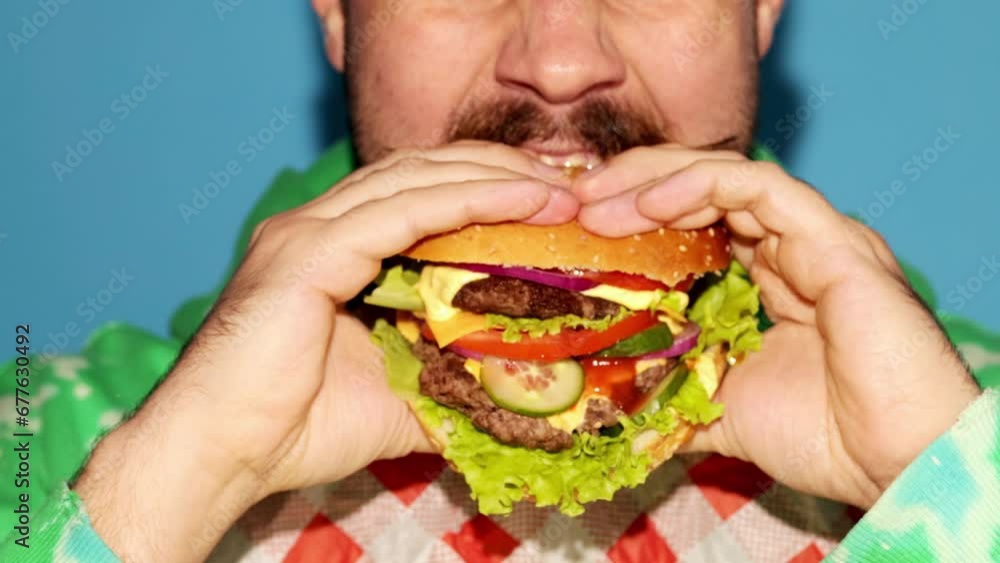 Cropped male face. Man eating freshly made, delicious burger with meat, cheese, salad and vegetables against colorful background. Concept of fast food, taste, junk food. Complementary colors. Ad Cropped male face. Man eating freshly made, delicious burger with meat, cheese, salad and vegetables against colorful background. Concept of fast food, taste, junk food. Complementary colors. Ad