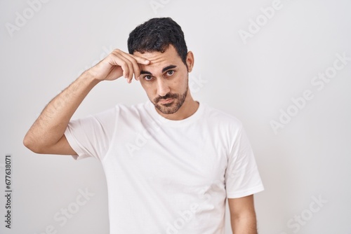 Handsome hispanic man standing over white background pointing unhappy to pimple on forehead, ugly infection of blackhead. acne and skin problem photo