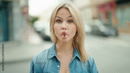 Young blonde woman smiling confident doing funny gesture with mouth at street