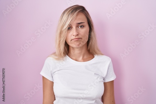 Young blonde woman standing over pink background depressed and worry for distress, crying angry and afraid. sad expression.