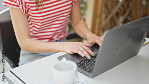 Young blonde woman using laptop sitting on table at coffee shop terrace