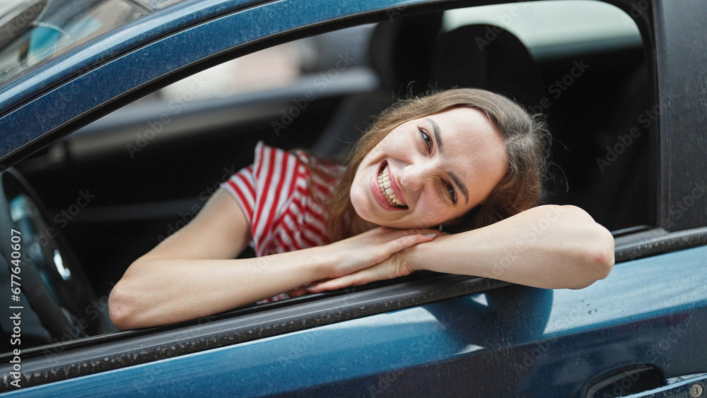 Young blonde woman smiling confident sitting on car at street