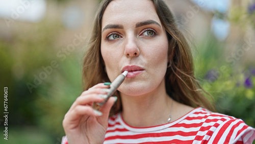 Young blonde woman smoking vaper at park