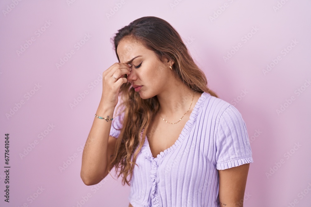 Young hispanic woman standing over pink background tired rubbing nose and eyes feeling fatigue and headache. stress and frustration concept. Young hispanic woman standing over pink background tired rubbing nose and eyes feeling fatigue and headache. stress and frustration concept.