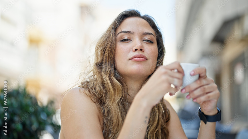 Young beautiful hispanic woman sitting on table holding cup coffee at coffee shop terrace Young beautiful hispanic woman sitting on table holding cup coffee at coffee shop terrace