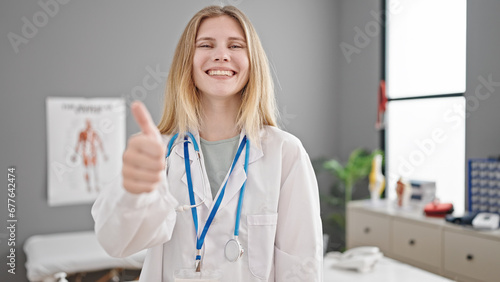 Young blonde woman doctor doing thumbs up smiling at clinic