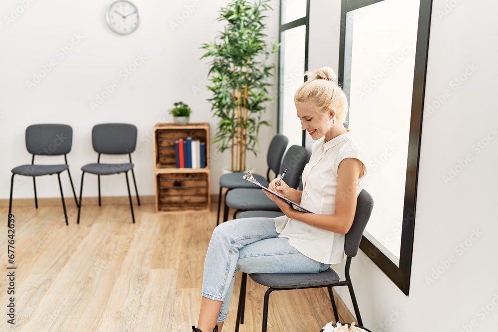 Young blonde woman using smartphone sitting on chair at waiting room Young blonde woman using smartphone sitting on chair at waiting room