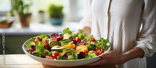 The woman prepared a delicious and healthy breakfast salad using fresh fruits in her white kitchen as she believed in maintaining her health and beauty through a balanced and nutritious diet