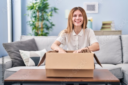 Young blonde woman unpacking cardboard box at home