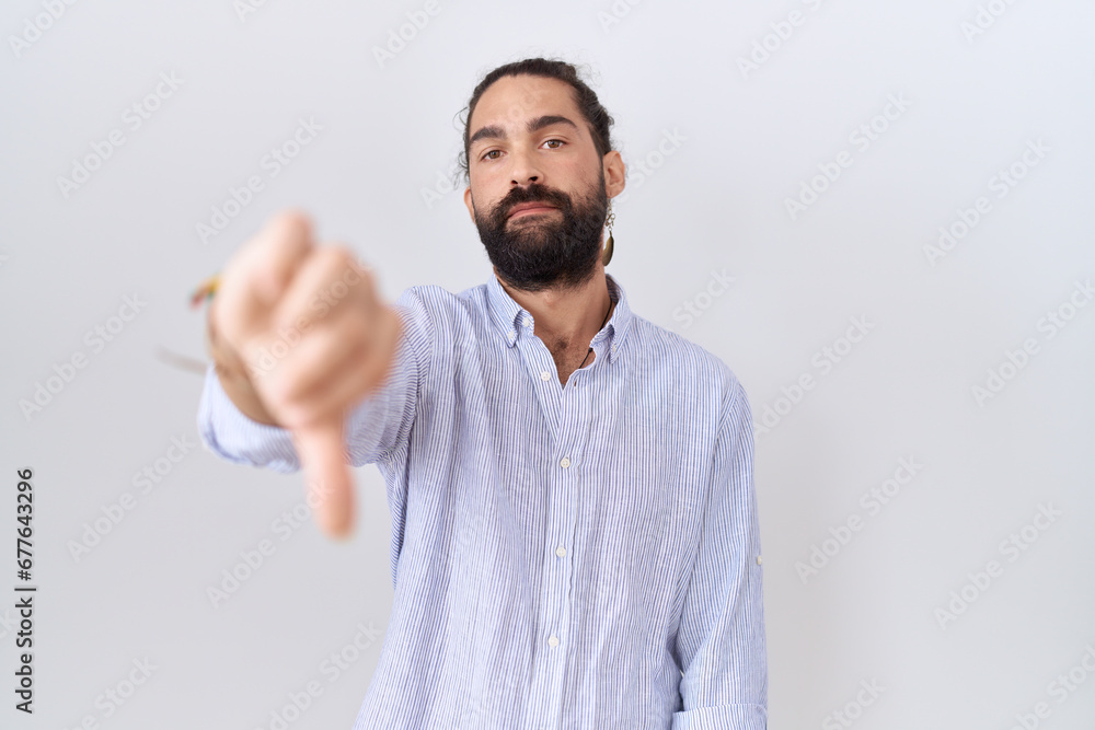 Hispanic man with beard wearing casual shirt looking unhappy and angry showing rejection and negative with thumbs down gesture. bad expression. Hispanic man with beard wearing casual shirt looking unhappy and angry showing rejection and negative with thumbs down gesture. bad expression.