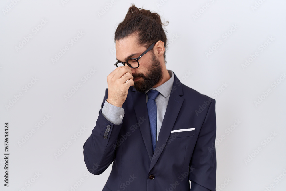 Hispanic man with beard wearing suit and tie tired rubbing nose and eyes feeling fatigue and headache. stress and frustration concept. Hispanic man with beard wearing suit and tie tired rubbing nose and eyes feeling fatigue and headache. stress and frustration concept.