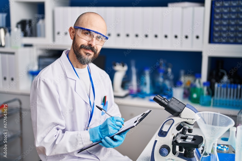 Young bald man scientist writing report working at laboratory Young bald man scientist writing report working at laboratory