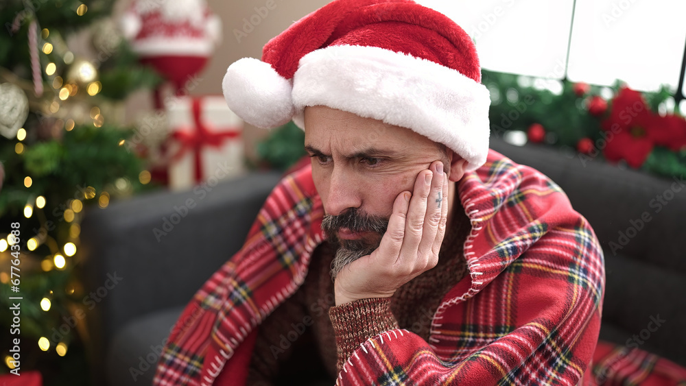 Young bald man sitting by christmas tree looking upset at home Young bald man sitting by christmas tree looking upset at home