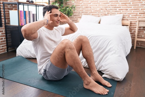 Young hispanic man smiling confident training abs exercise at bedroom